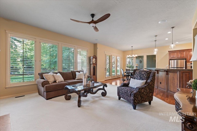 carpeted living room featuring a textured ceiling and ceiling fan with notable chandelier