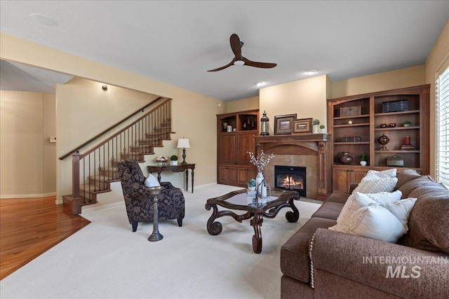 living room featuring a tile fireplace, light hardwood / wood-style floors, and ceiling fan