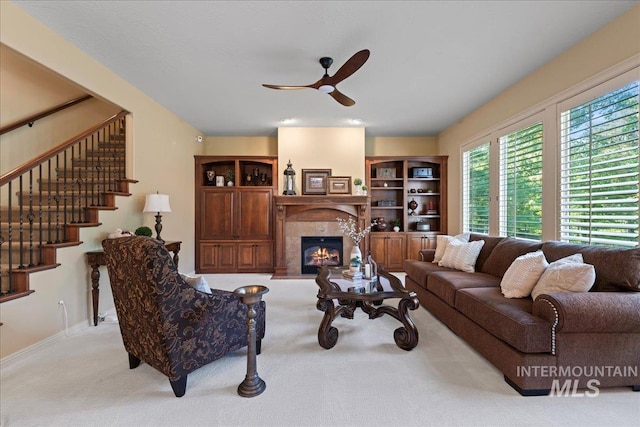 living room with a tile fireplace, ceiling fan, and light colored carpet