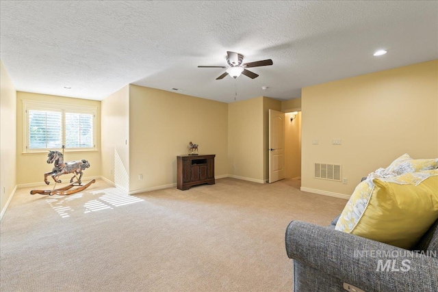 sitting room with ceiling fan, light colored carpet, and a textured ceiling