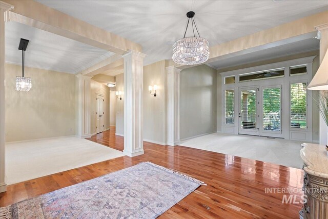 interior space with wood-type flooring, ornamental molding, ceiling fan with notable chandelier, and ornate columns