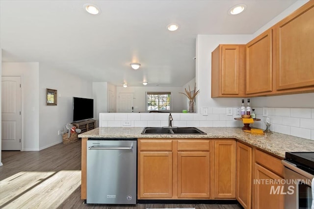 kitchen featuring a peninsula, light stone countertops, a sink, light wood finished floors, and appliances with stainless steel finishes
