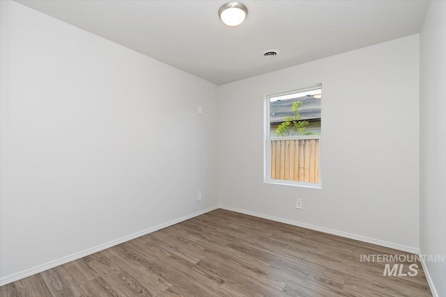 unfurnished room with baseboards, visible vents, and wood finished floors