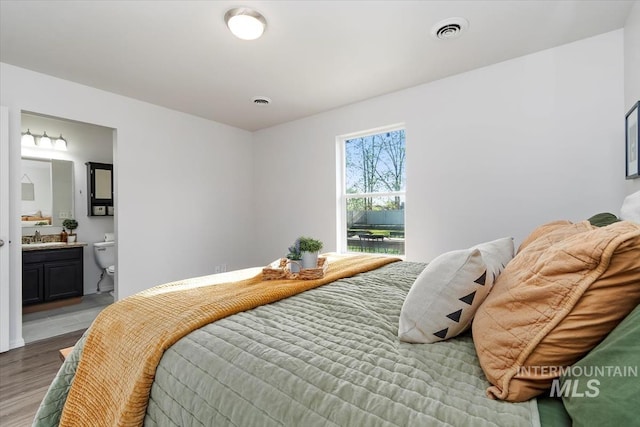 bedroom with connected bathroom, visible vents, a sink, and wood finished floors