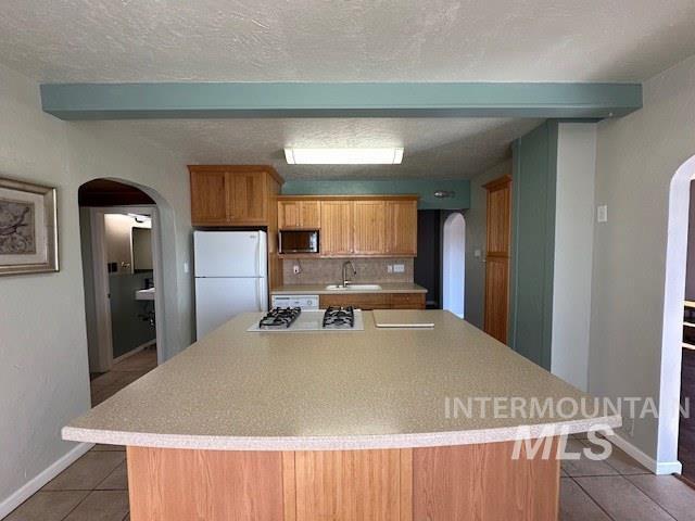 kitchen featuring arched walkways, light countertops, white appliances, and dark tile patterned floors