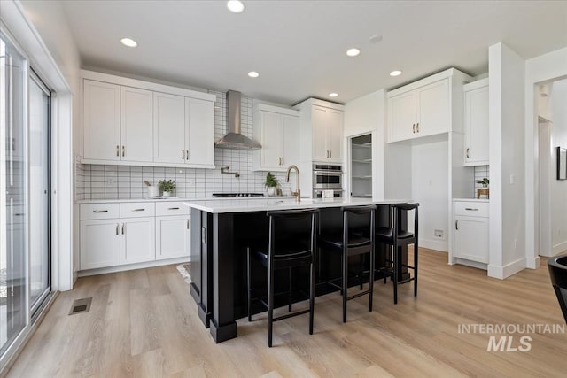 kitchen with light countertops, wall chimney range hood, light wood-style flooring, and visible vents