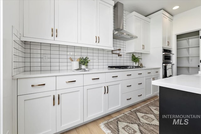 kitchen with stainless steel appliances, wall chimney range hood, light countertops, and white cabinetry