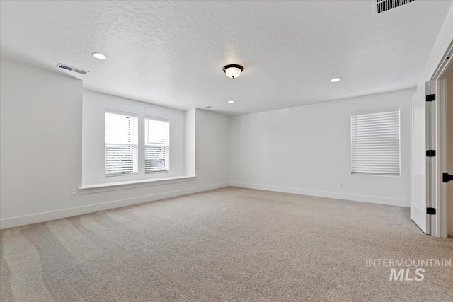 empty room featuring light carpet, a textured ceiling, visible vents, and baseboards