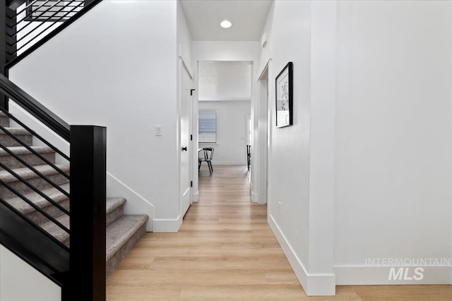 hallway featuring light wood finished floors, stairs, and baseboards