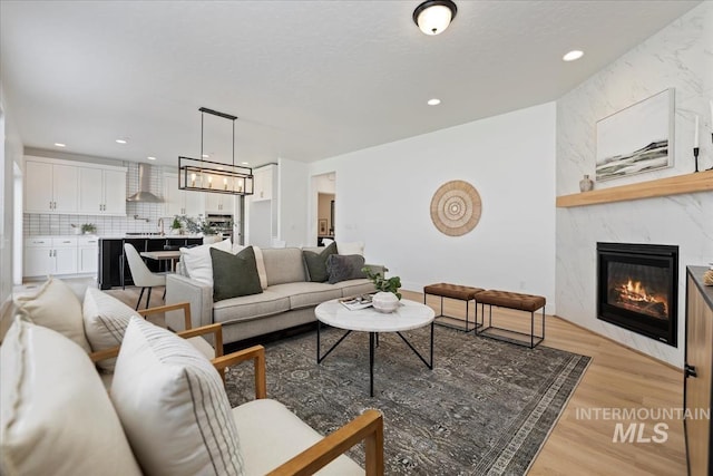 living room with a textured ceiling, recessed lighting, a notable chandelier, a premium fireplace, and light wood-style floors