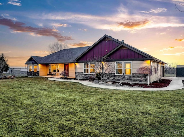 back of house at dusk with a yard, stone siding, and board and batten siding