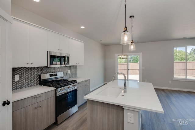 kitchen featuring backsplash, stainless steel appliances, sink, pendant lighting, and an island with sink