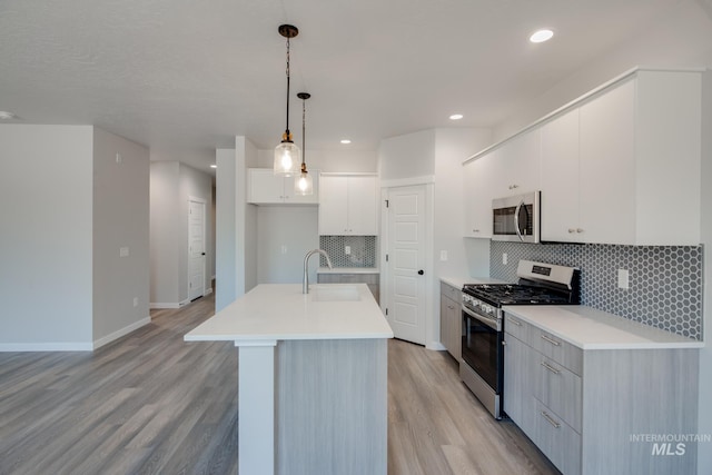 kitchen featuring appliances with stainless steel finishes, a kitchen island with sink, sink, decorative light fixtures, and white cabinetry