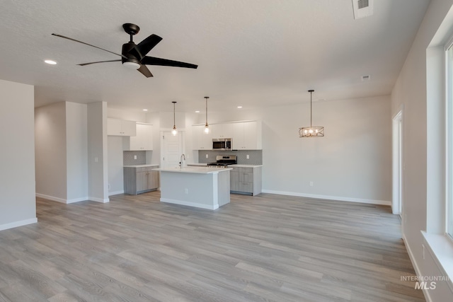 kitchen with white cabinetry, stainless steel appliances, hanging light fixtures, tasteful backsplash, and an island with sink