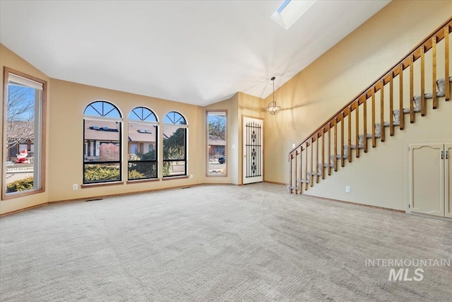 unfurnished living room featuring a chandelier, lofted ceiling with skylight, and carpet floors