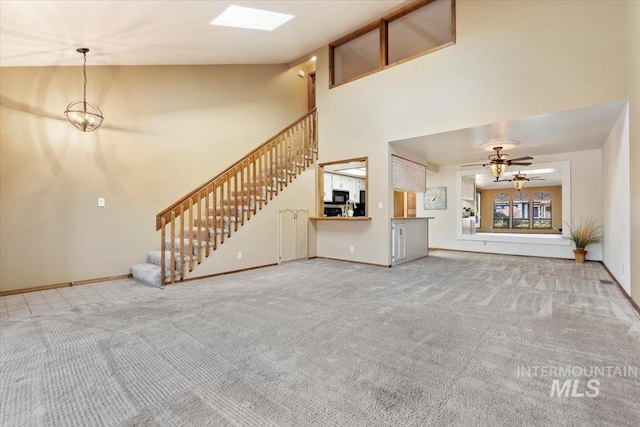 unfurnished living room featuring carpet floors, lofted ceiling with skylight, and ceiling fan with notable chandelier