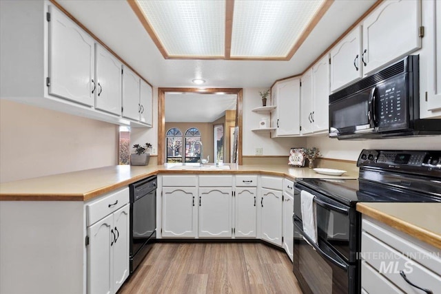 kitchen with white cabinetry, kitchen peninsula, black appliances, light hardwood / wood-style flooring, and sink