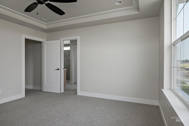 empty room with a tray ceiling, ceiling fan, and carpet floors