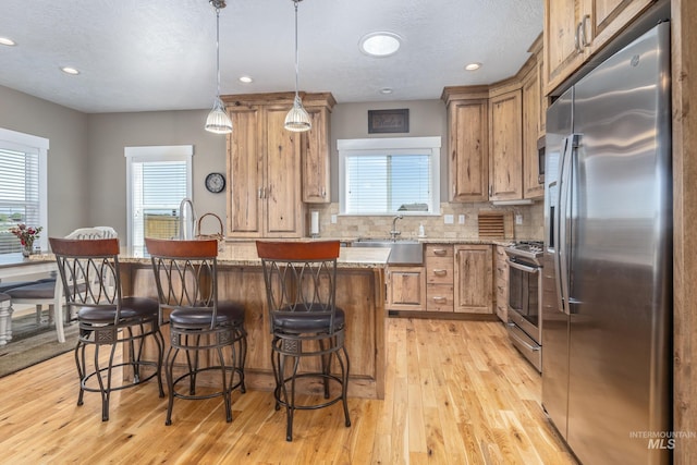 120 S Marko Ln, Kuna, ID 83634 - kitchen with appliances with stainless steel finishes, a sink, a breakfast bar, light wood finished floors, and decorative backsplash