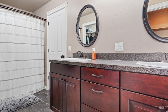 full bathroom featuring stone finish flooring, double vanity, a shower with shower curtain, and a sink