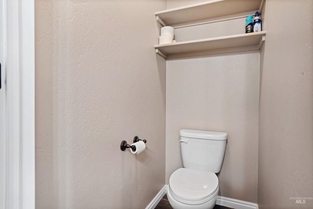 half bath with toilet, baseboards, and a textured wall