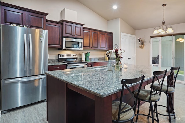 kitchen with appliances with stainless steel finishes, a kitchen island with sink, vaulted ceiling, stone counters, and a sink