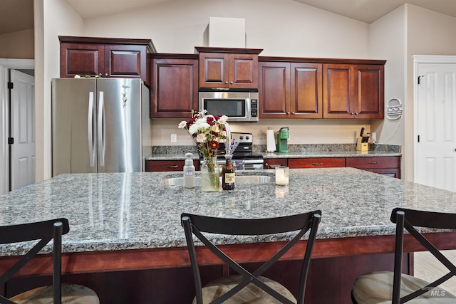 kitchen with appliances with stainless steel finishes, a breakfast bar, stone countertops, and vaulted ceiling