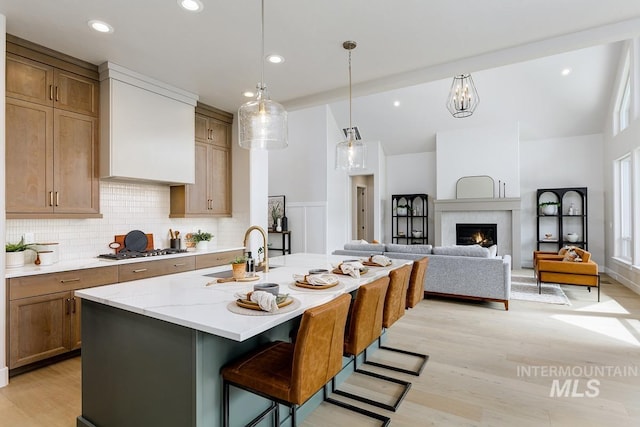 kitchen with a sink, light wood-type flooring, a kitchen island with sink, backsplash, and stainless steel gas cooktop