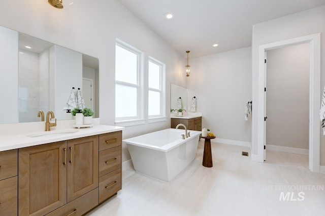 full bath featuring two vanities, a freestanding tub, recessed lighting, a sink, and baseboards