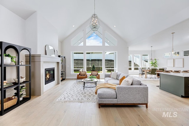 living area featuring light wood-style flooring, high vaulted ceiling, and a tiled fireplace
