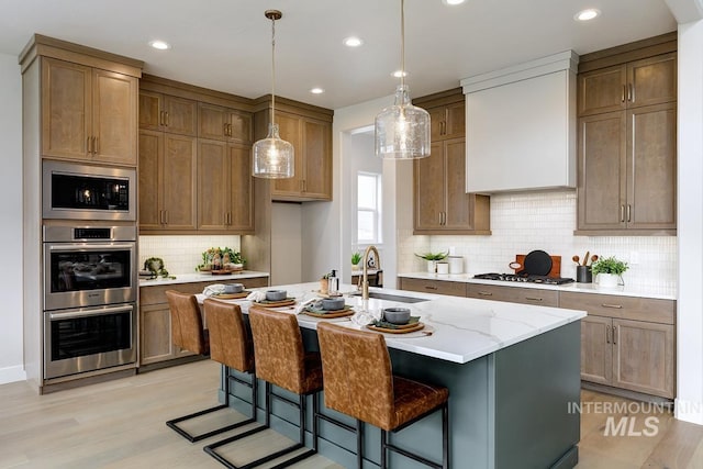 kitchen with decorative light fixtures, a sink, appliances with stainless steel finishes, a center island with sink, and backsplash