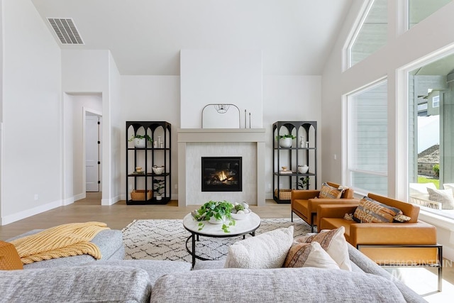 living room with visible vents, baseboards, wood finished floors, high vaulted ceiling, and a glass covered fireplace