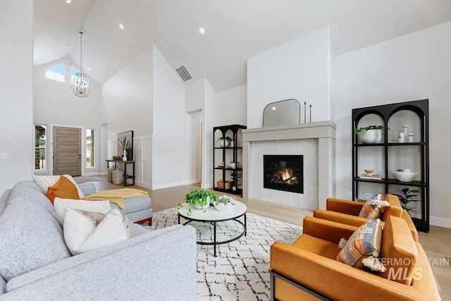living area with a glass covered fireplace, light wood-type flooring, baseboards, visible vents, and high vaulted ceiling