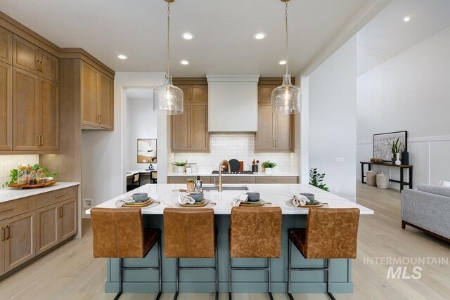 kitchen with light wood-style flooring, a kitchen bar, pendant lighting, custom range hood, and a wainscoted wall