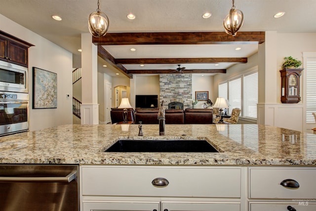 kitchen with sink, ceiling fan, appliances with stainless steel finishes, a fireplace, and decorative light fixtures