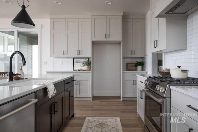 kitchen featuring pendant lighting, stainless steel appliances, a sink, light wood-type flooring, and wall chimney exhaust hood