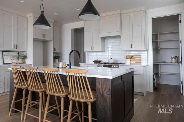 kitchen with a kitchen island with sink, wood finished floors, light countertops, tasteful backsplash, and pendant lighting