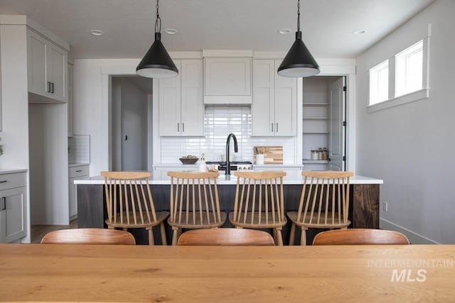 kitchen featuring decorative light fixtures, a center island with sink, tasteful backsplash, light countertops, and a kitchen bar