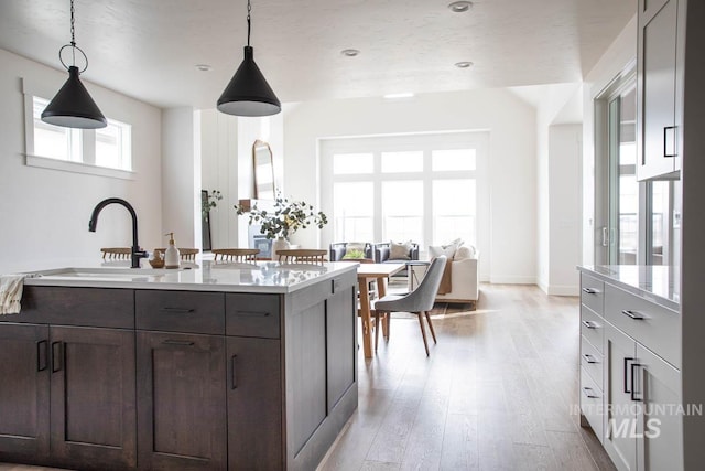 kitchen featuring light wood-style flooring, hanging light fixtures, light countertops, dark brown cabinets, and a sink