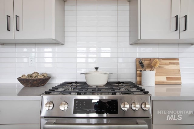 kitchen featuring stainless steel gas stove, white cabinets, decorative backsplash, and light countertops