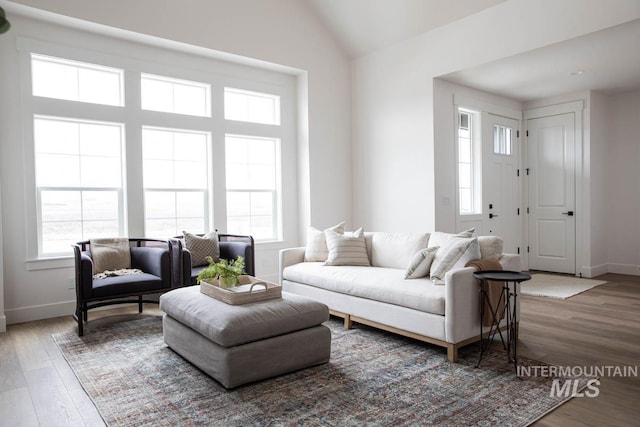 living area with baseboards, vaulted ceiling, and wood finished floors