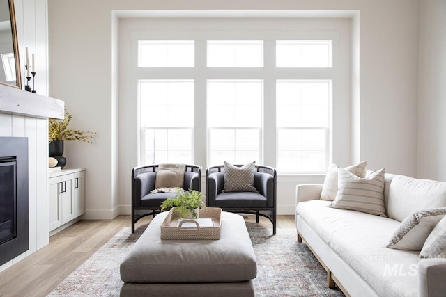 living area with a glass covered fireplace, light wood-style flooring, and baseboards