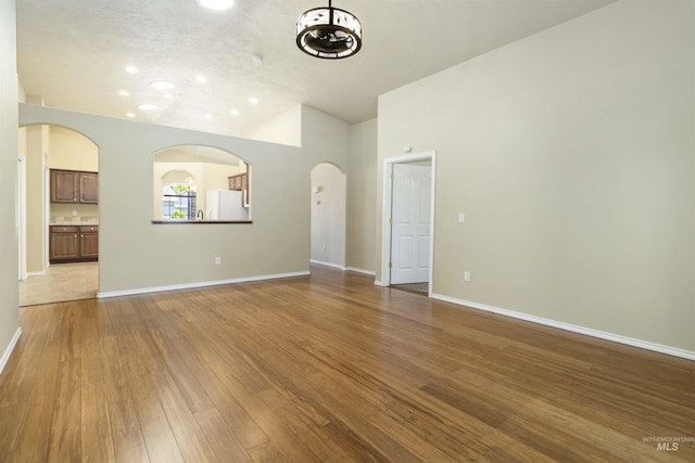421 N David Frost St, Nampa, ID 83651 - unfurnished living room featuring hardwood / wood-style floors, baseboards, arched walkways, high vaulted ceiling, and recessed lighting