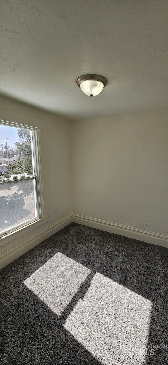 unfurnished room featuring dark colored carpet and baseboards