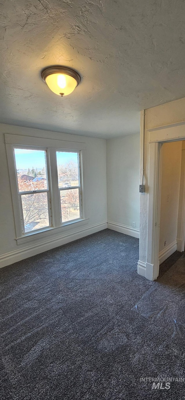 spare room featuring a textured ceiling, baseboards, and dark colored carpet