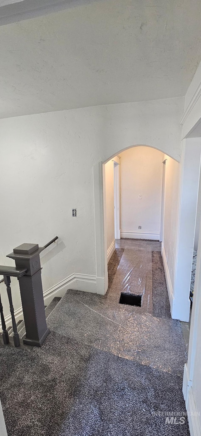 interior space featuring arched walkways, a textured ceiling, baseboards, and vaulted ceiling