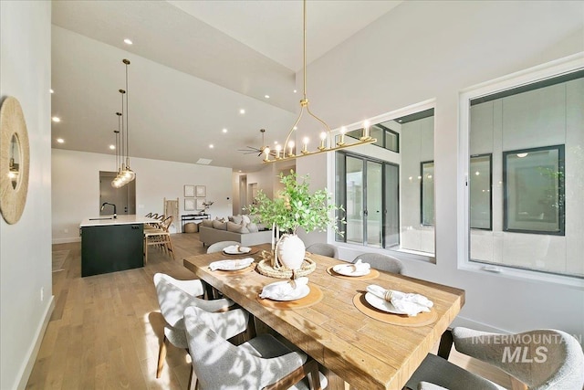 dining space with sink, high vaulted ceiling, an inviting chandelier, and hardwood / wood-style flooring