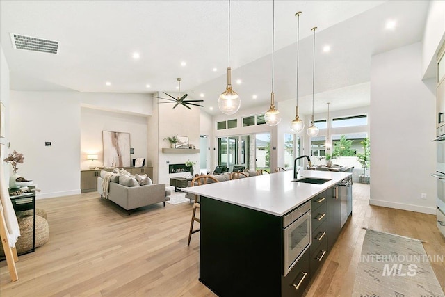 kitchen featuring stainless steel microwave, sink, light hardwood / wood-style flooring, pendant lighting, and a center island with sink