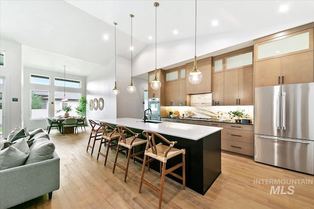 kitchen featuring hanging light fixtures, stainless steel appliances, a kitchen breakfast bar, backsplash, and an island with sink