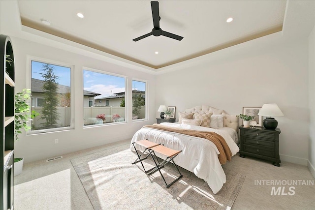 carpeted bedroom featuring a tray ceiling and ceiling fan